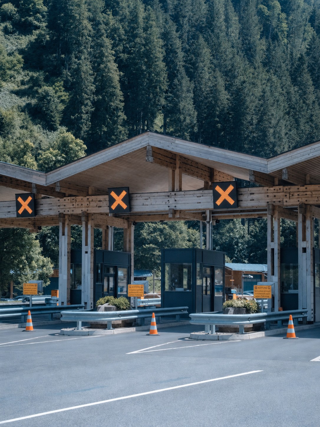 A covered checkpoint structure with a wood-beam roof, set against a forested mountainside